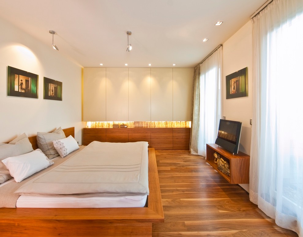 Imagen de dormitorio principal actual grande sin chimenea con paredes blancas y suelo de madera en tonos medios
