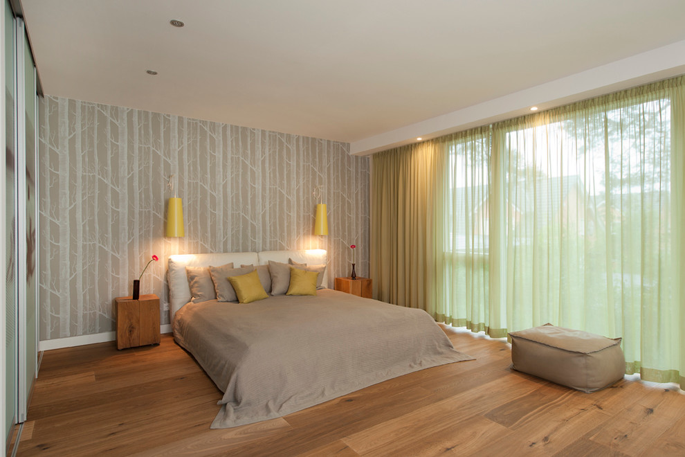Modelo de dormitorio principal actual grande sin chimenea con paredes blancas y suelo de madera en tonos medios