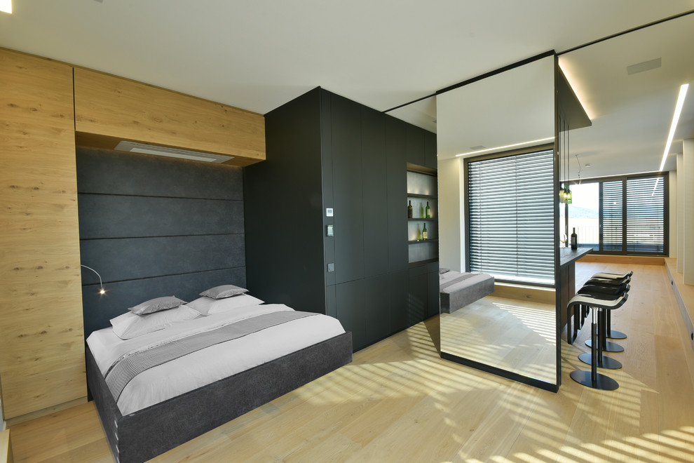 Modelo de dormitorio tipo loft actual grande sin chimenea con paredes blancas, suelo de madera clara y suelo marrón