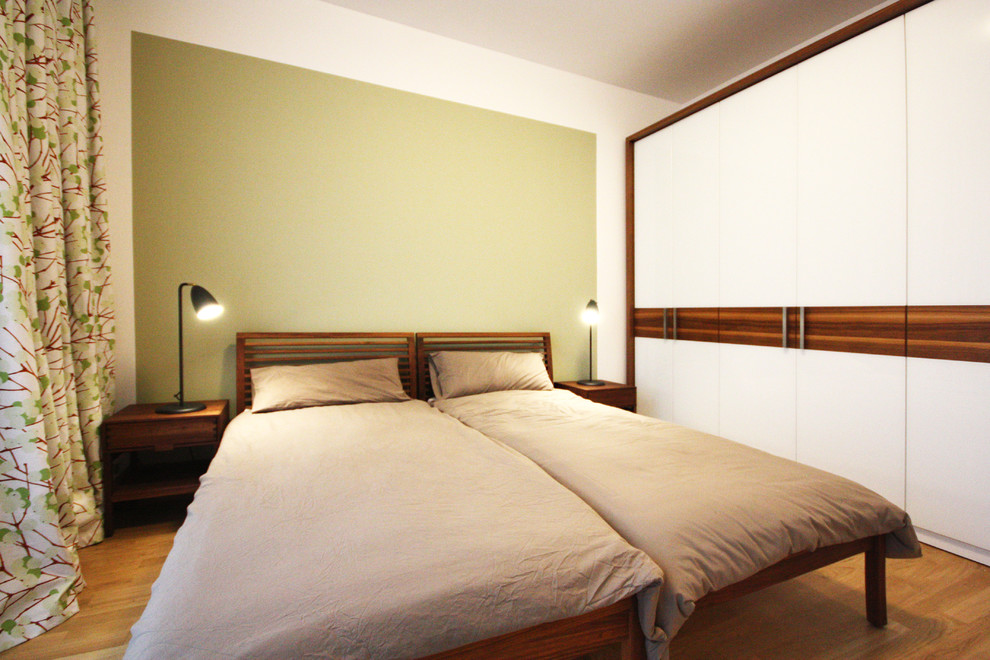 Modernes Schlafzimmer ohne Kamin mit grüner Wandfarbe und braunem Holzboden in Berlin