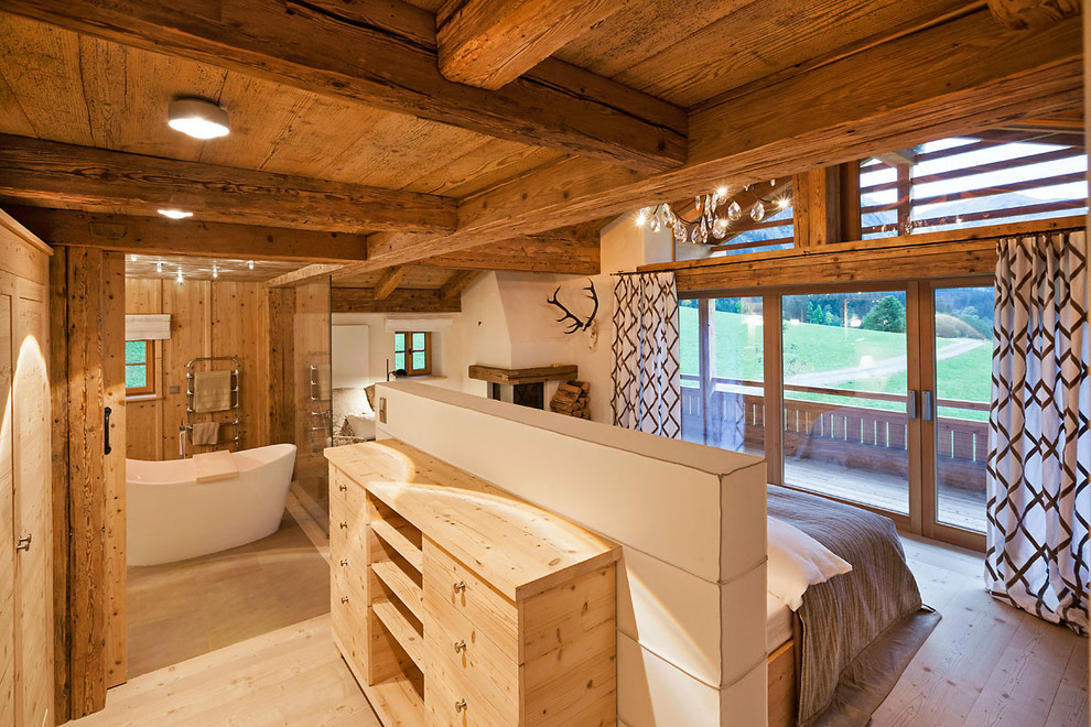 На фото: хозяйская спальня среднего размера в стиле рустика с белыми стенами, светлым паркетным полом, угловым камином, фасадом камина из штукатурки и коричневым полом