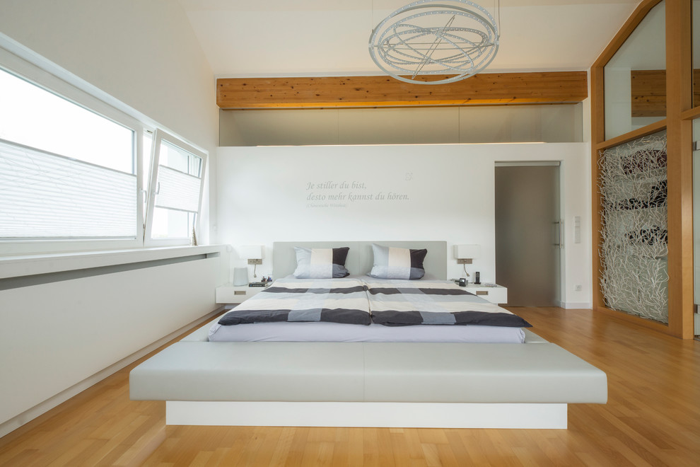 Großes Modernes Schlafzimmer ohne Kamin mit weißer Wandfarbe und braunem Holzboden in Nürnberg