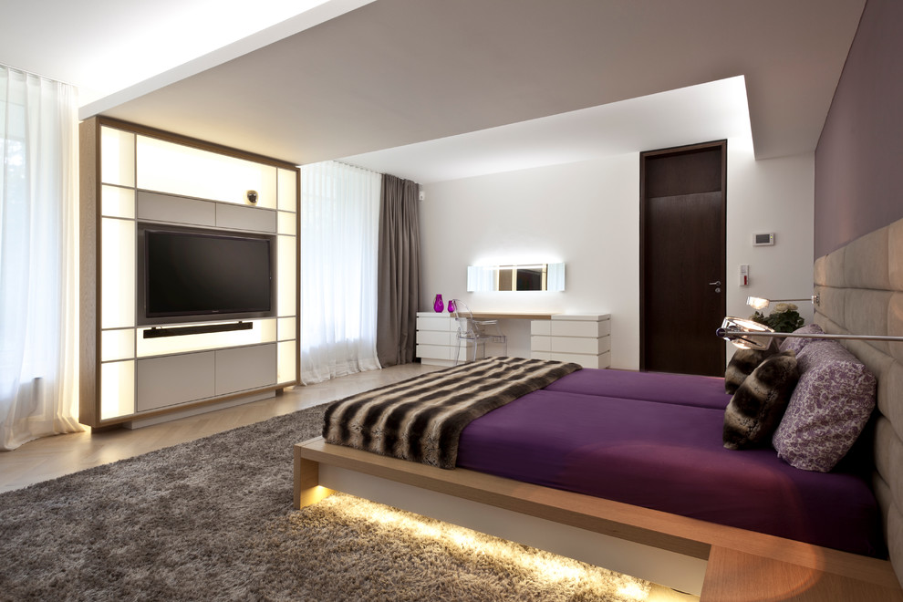 Modelo de dormitorio contemporáneo grande sin chimenea con paredes blancas, suelo de madera clara y con escritorio
