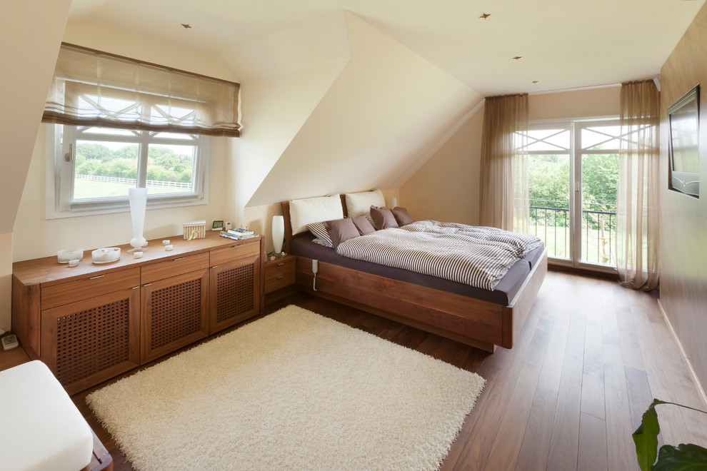 Imagen de dormitorio principal actual grande sin chimenea con paredes beige, suelo de madera en tonos medios y techo inclinado