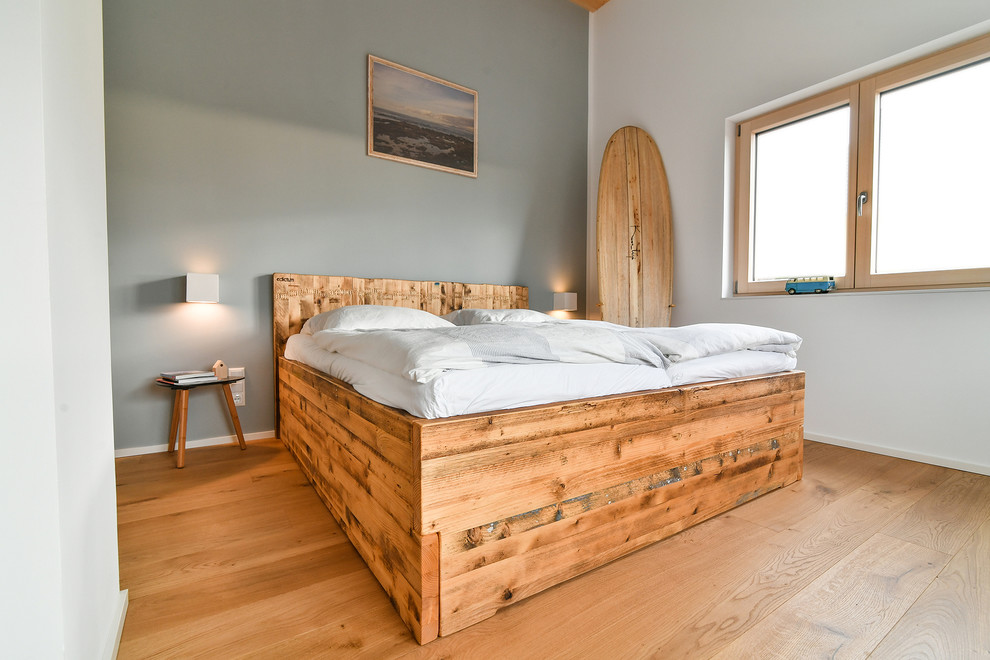 Foto de dormitorio principal moderno grande con paredes grises, suelo de madera clara, estufa de leña, marco de chimenea de ladrillo y suelo marrón