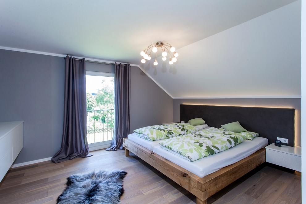 Cette image montre une chambre parentale design de taille moyenne avec un mur gris, parquet foncé et un sol marron.