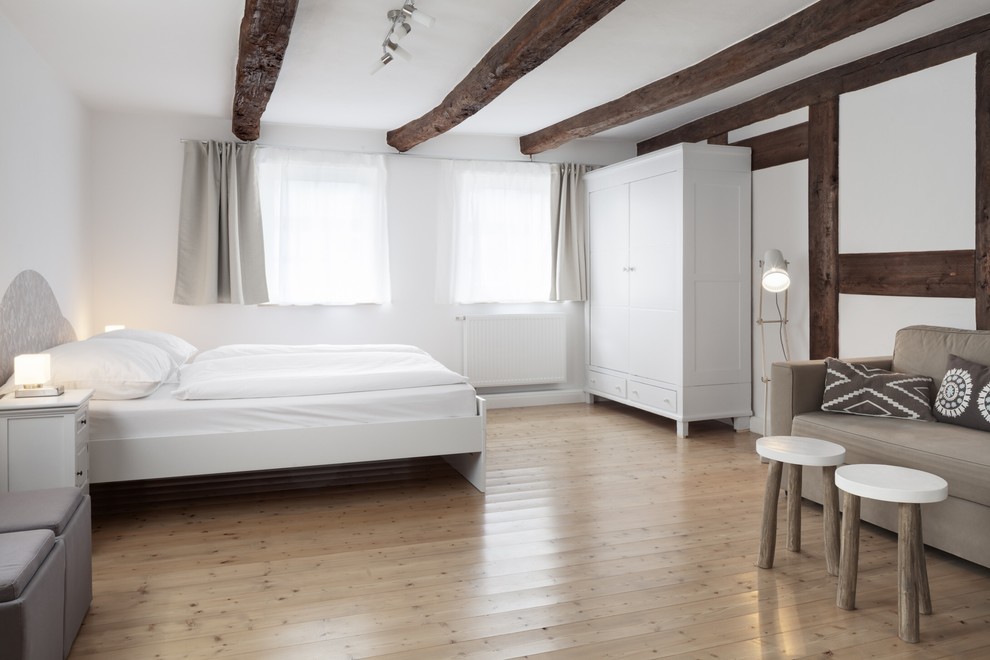 Modelo de dormitorio principal de estilo de casa de campo grande sin chimenea con paredes blancas y suelo de madera clara