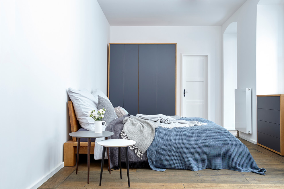 Ejemplo de dormitorio principal nórdico de tamaño medio sin chimenea con paredes blancas, suelo de madera pintada y suelo marrón