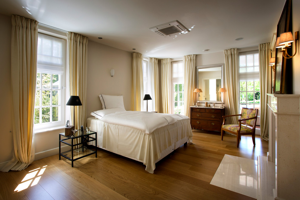 Großes Hauptschlafzimmer mit beiger Wandfarbe, braunem Holzboden, Kamin und Kaminumrandung aus Stein in Köln