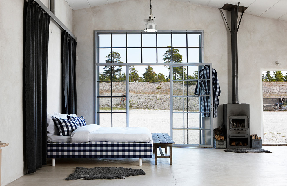 На фото: спальня среднего размера в стиле лофт с печью-буржуйкой, бетонным полом и серыми стенами с