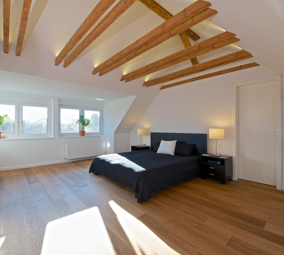 Imagen de dormitorio contemporáneo grande sin chimenea con paredes blancas, suelo de madera clara y techo inclinado