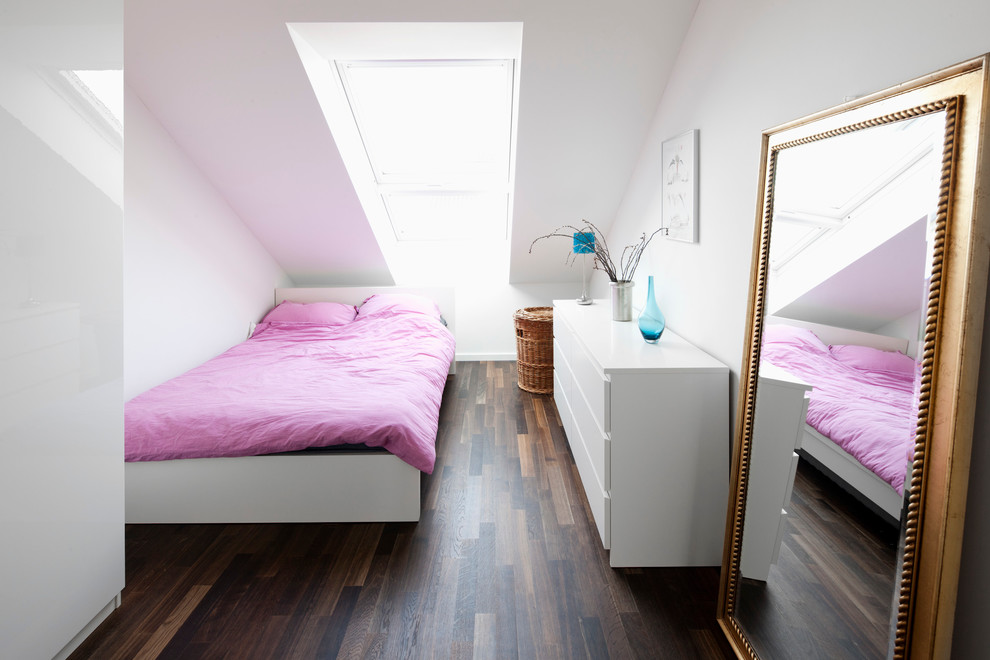 Modelo de dormitorio contemporáneo pequeño sin chimenea con paredes blancas, suelo de madera oscura y techo inclinado