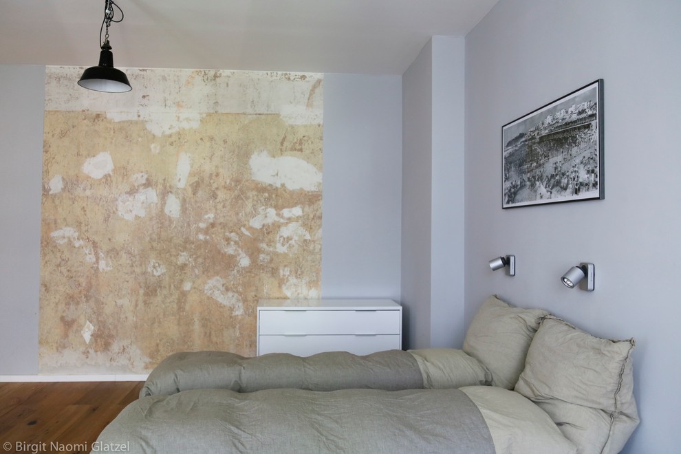 Exemple d'une petite chambre mansardée ou avec mezzanine industrielle avec un mur gris et un sol en bois brun.