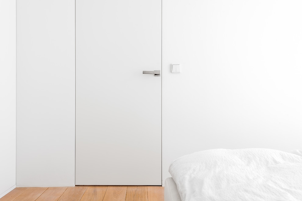 Idée de décoration pour une chambre mansardée ou avec mezzanine minimaliste de taille moyenne avec un mur blanc et parquet clair.