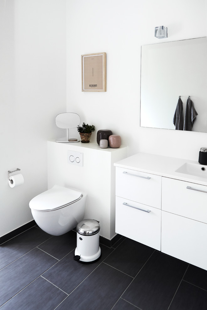 Idéer för mellanstora nordiska toaletter, med släta luckor, vita skåp, en vägghängd toalettstol, vita väggar, klinkergolv i keramik, ett integrerad handfat, laminatbänkskiva och grått golv