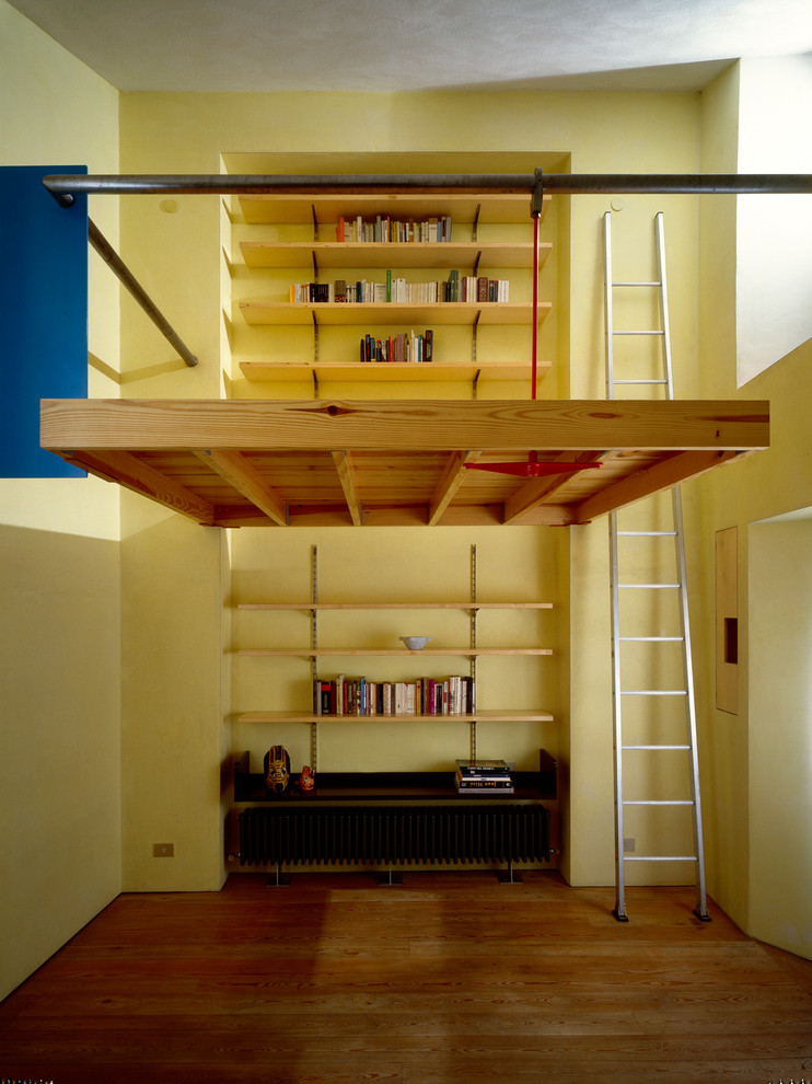 Immagine di un piccolo soggiorno minimal aperto con libreria, pareti gialle e pavimento in legno massello medio