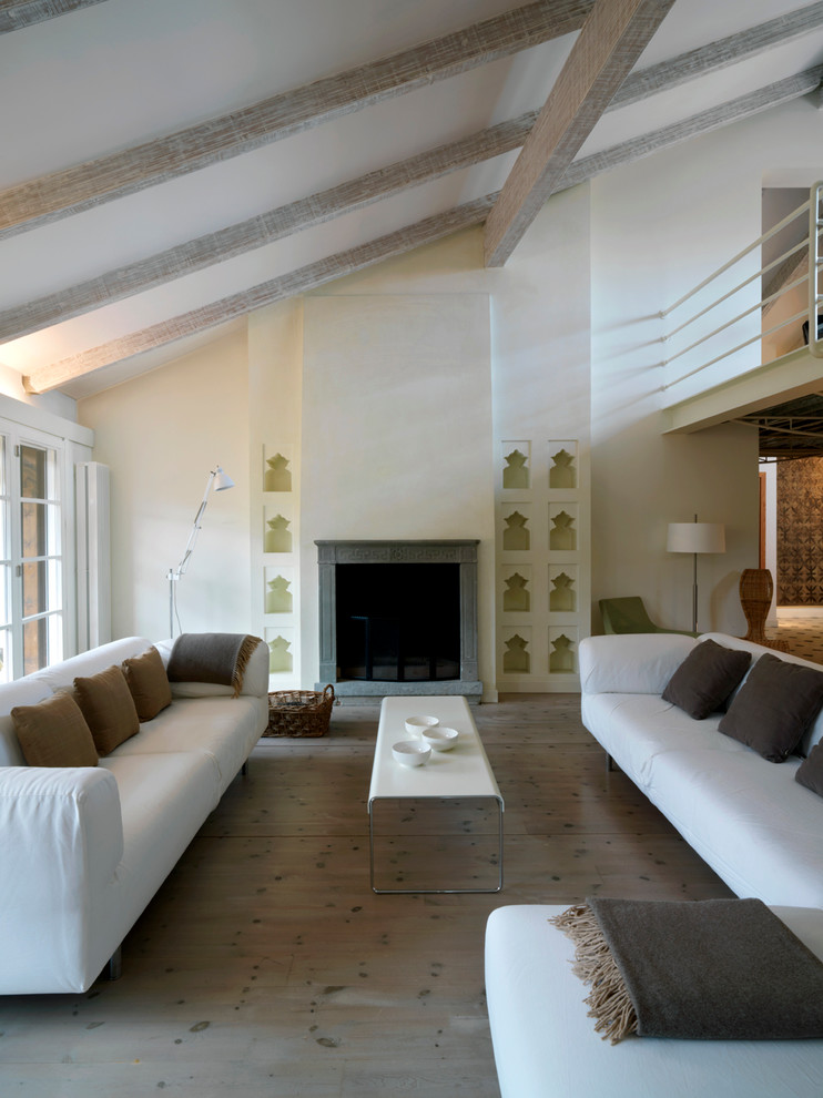 Modelo de salón abierto mediterráneo grande con paredes blancas, suelo de madera clara, todas las chimeneas y marco de chimenea de piedra