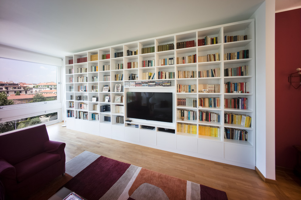 Ejemplo de biblioteca en casa actual de tamaño medio con paredes blancas, suelo de madera en tonos medios y pared multimedia