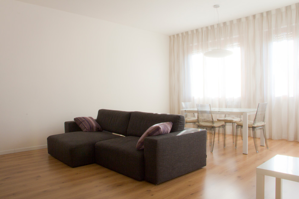 Ejemplo de salón abierto actual de tamaño medio sin chimenea con paredes blancas, suelo de madera clara, televisor colgado en la pared y suelo beige