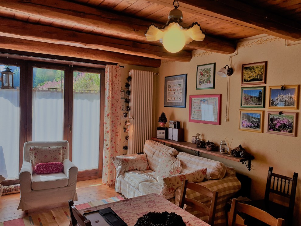 Ejemplo de salón cerrado rústico pequeño con paredes amarillas, suelo de madera clara, estufa de leña, marco de chimenea de metal y suelo marrón