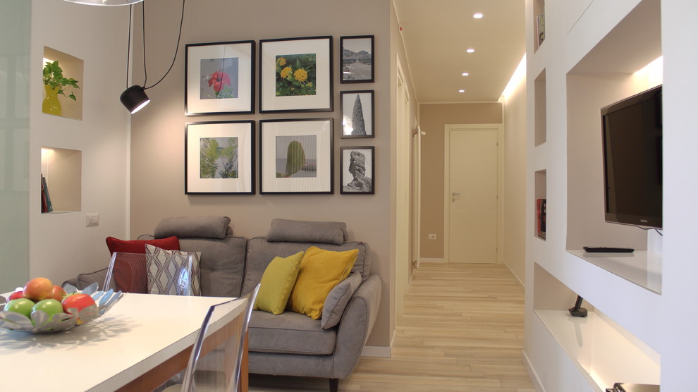 Пример оригинального дизайна: маленькая открытая гостиная комната в скандинавском стиле с с книжными шкафами и полками, бежевыми стенами, полом из керамогранита и телевизором на стене для на участке и в саду
