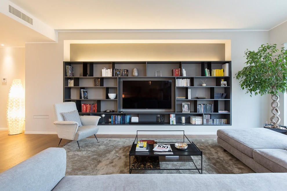 Ejemplo de biblioteca en casa abierta actual grande con paredes grises, suelo de madera oscura, televisor colgado en la pared y suelo marrón