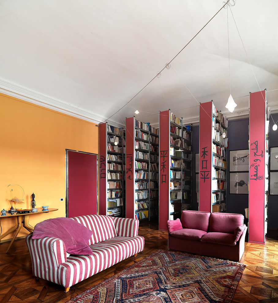 Cette image montre une très grande salle de séjour bohème fermée avec une bibliothèque ou un coin lecture, un mur multicolore et un sol en bois brun.