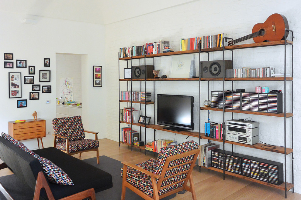 Modelo de biblioteca en casa abierta retro de tamaño medio con paredes blancas, suelo de madera clara y pared multimedia