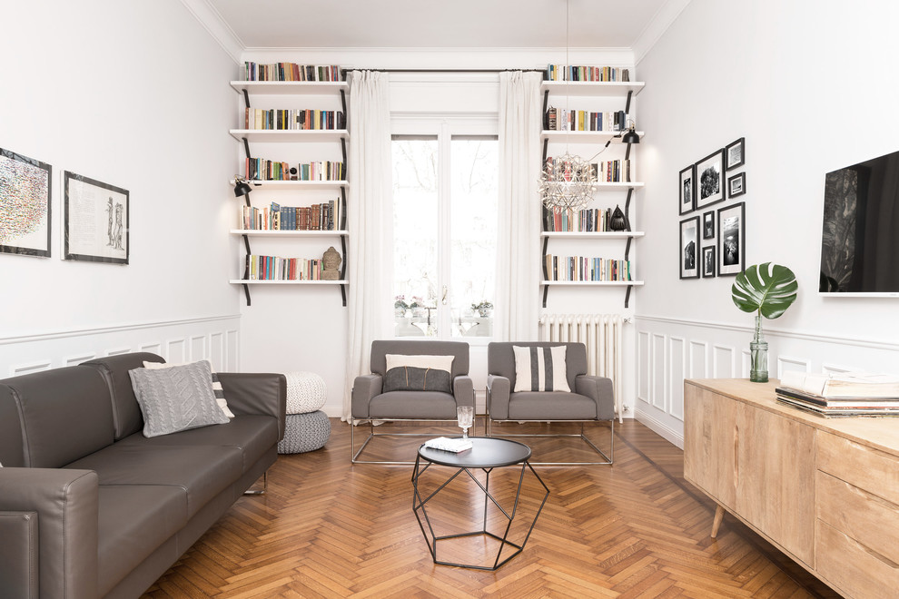 Réalisation d'un salon gris et blanc nordique de taille moyenne avec une bibliothèque ou un coin lecture, un téléviseur fixé au mur, un mur blanc, un sol en bois brun et un sol marron.