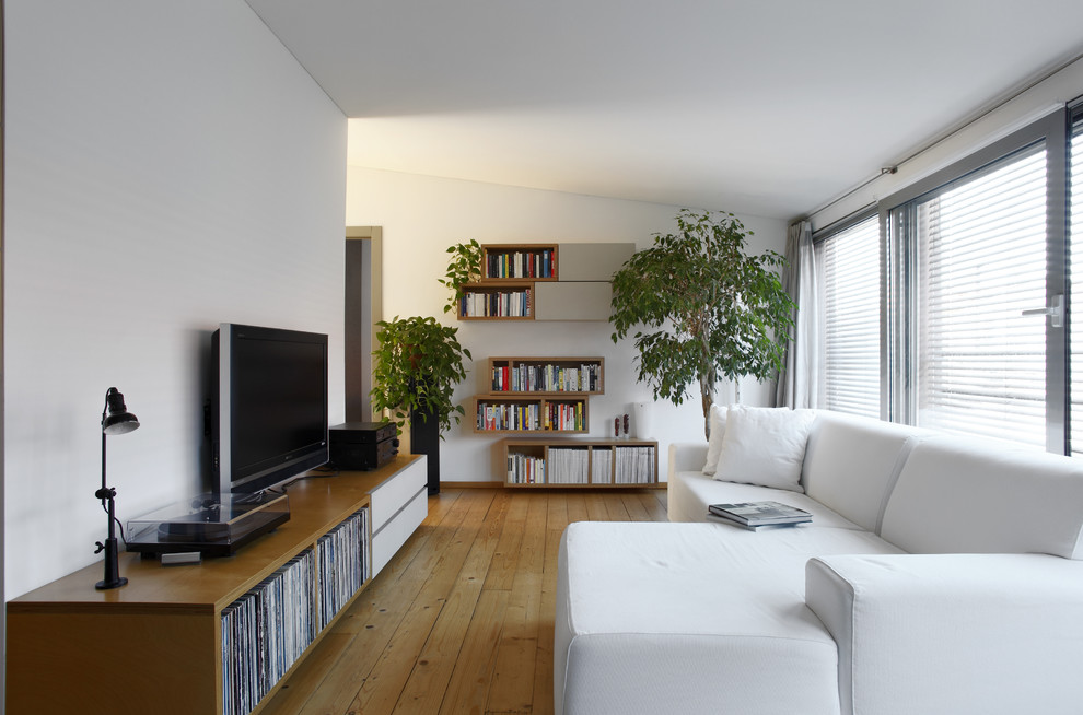 Idée de décoration pour une petite salle de séjour minimaliste fermée avec une bibliothèque ou un coin lecture, un mur blanc, un sol en bois brun, un téléviseur encastré et un sol marron.
