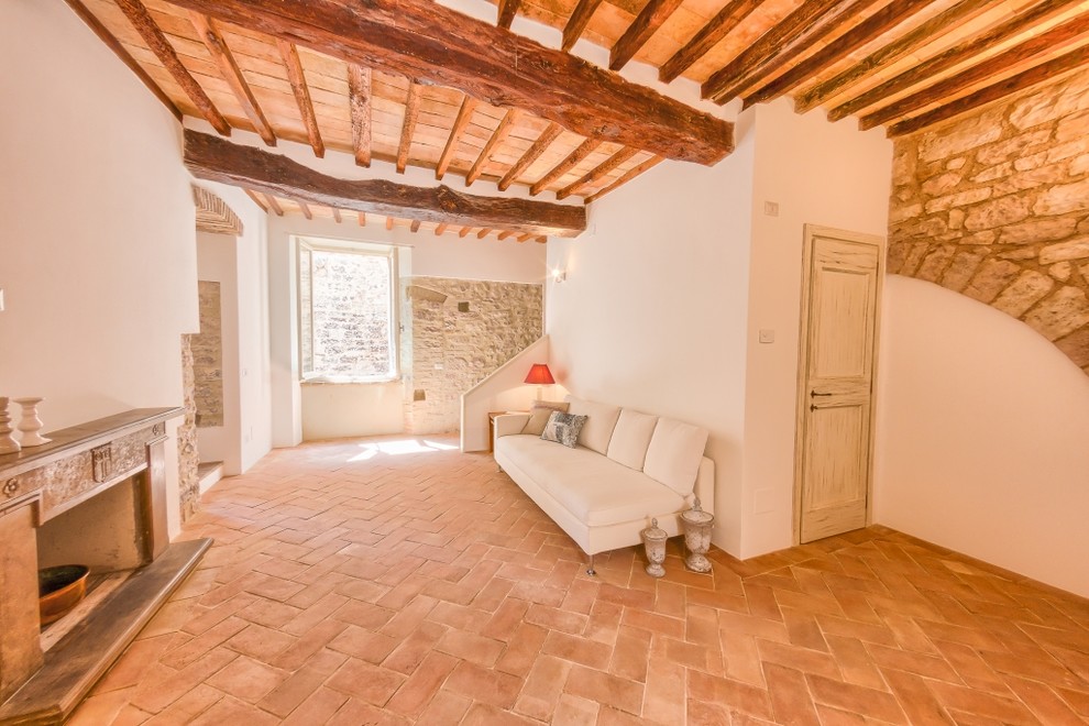 Exemple d'un salon méditerranéen de taille moyenne et fermé avec un mur blanc, tomettes au sol, une cheminée standard et un manteau de cheminée en pierre.