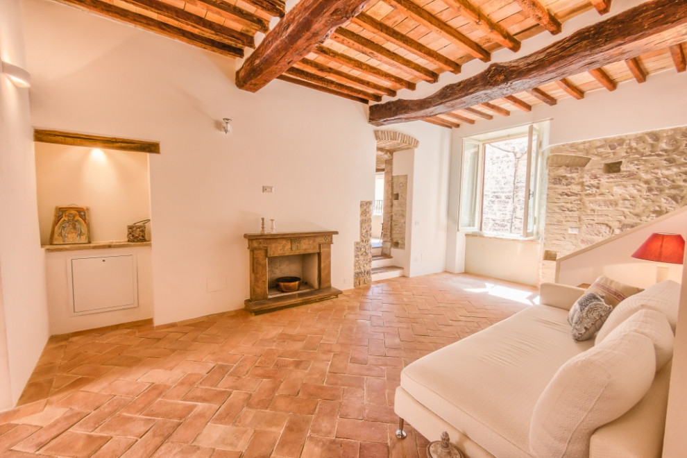 Foto de salón romántico de tamaño medio con paredes blancas, suelo de baldosas de terracota, todas las chimeneas y marco de chimenea de piedra