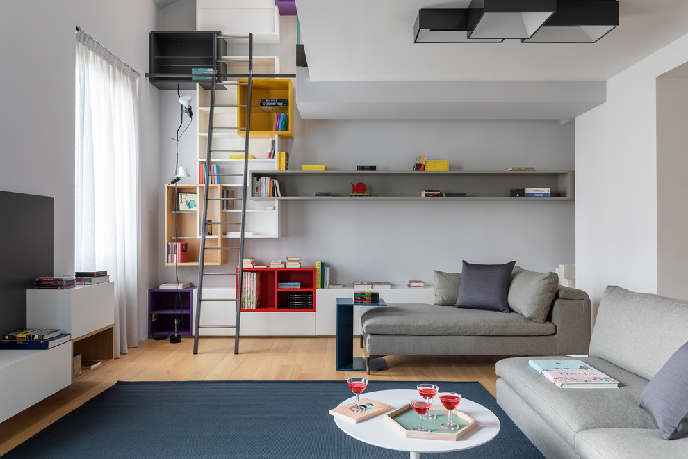 Immagine di un grande soggiorno design aperto con libreria, pareti grigie, pavimento in legno massello medio, TV a parete e pavimento marrone