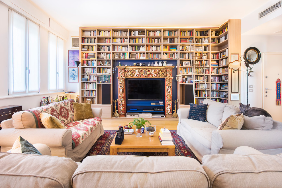 Inredning av ett medelhavsstil stort vardagsrum, med ett bibliotek, blå väggar, ljust trägolv, en standard öppen spis, en spiselkrans i trä och en dold TV