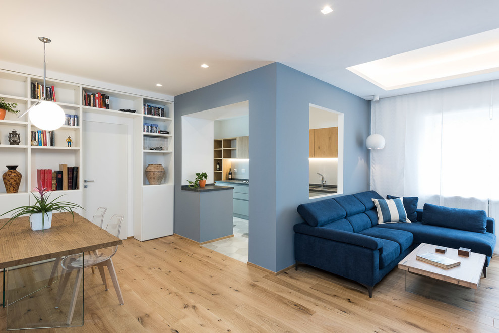 Пример оригинального дизайна: открытая гостиная комната в современном стиле с с книжными шкафами и полками, синими стенами, паркетным полом среднего тона, бежевым полом и синим диваном