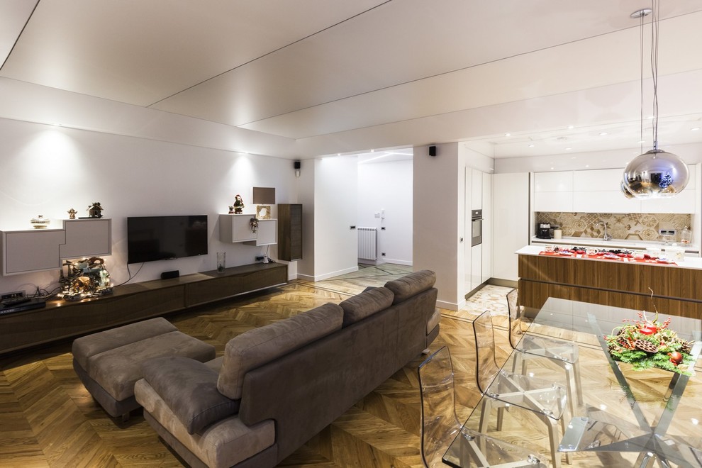 Стильный дизайн: огромная парадная, открытая гостиная комната в современном стиле с белыми стенами, паркетным полом среднего тона и телевизором на стене - последний тренд