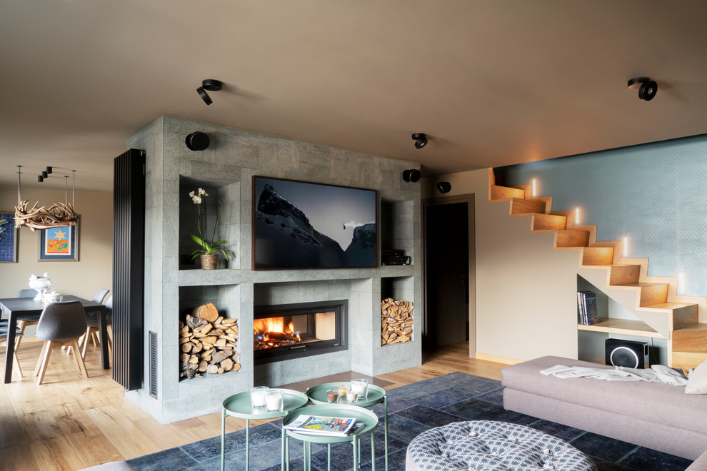 Diseño de salón abierto contemporáneo de tamaño medio con suelo de madera en tonos medios, estufa de leña, paredes azules, marco de chimenea de piedra, pared multimedia y suelo negro