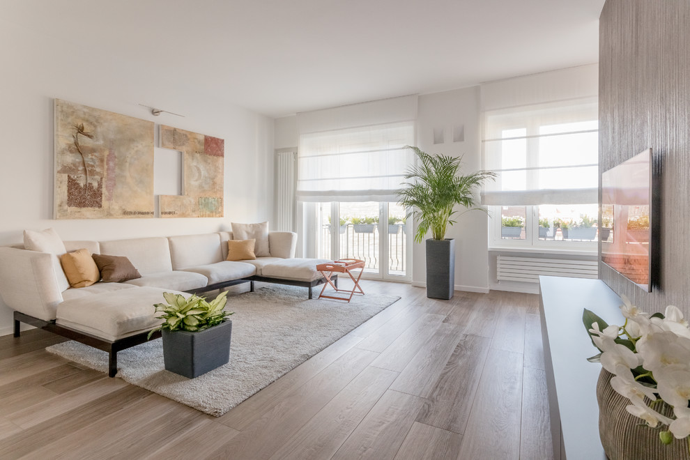 Modelo de salón abierto actual con paredes blancas, suelo de madera en tonos medios, televisor colgado en la pared, suelo marrón y alfombra