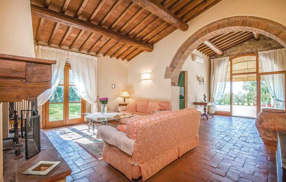 フィレンツェにある広いカントリー風のおしゃれなオープンリビング (テラコッタタイルの床、標準型暖炉、漆喰の暖炉まわり、据え置き型テレビ、赤い床) の写真