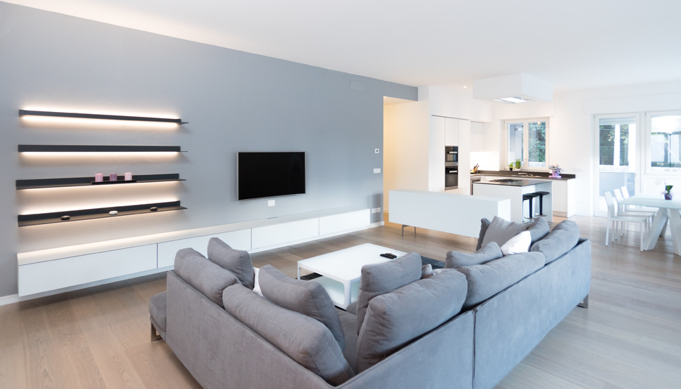 Esempio di un ampio soggiorno design aperto con pareti grigie, pavimento in legno massello medio e TV a parete