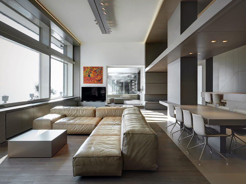 На фото: огромная открытая гостиная комната в современном стиле с отдельно стоящим телевизором, белыми стенами и светлым паркетным полом без камина