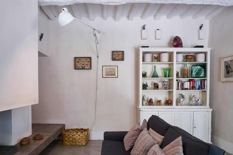 Diseño de sala de estar con biblioteca de estilo de casa de campo con paredes beige, marco de chimenea de yeso, suelo gris y chimeneas suspendidas