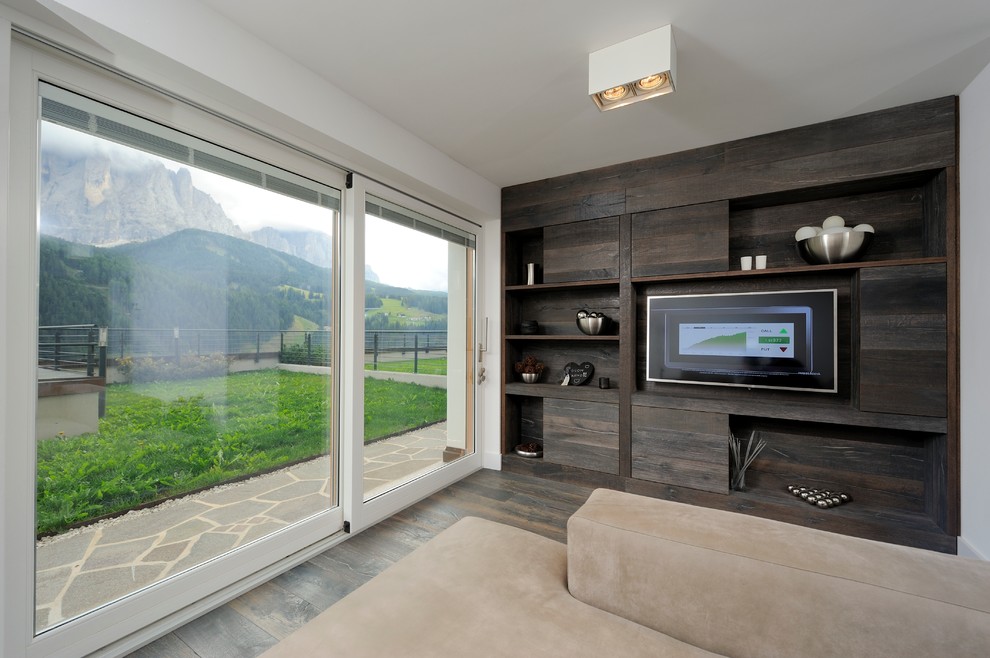 Immagine di un piccolo soggiorno minimal aperto con libreria, pareti multicolore, pavimento in legno massello medio, TV a parete e pavimento marrone
