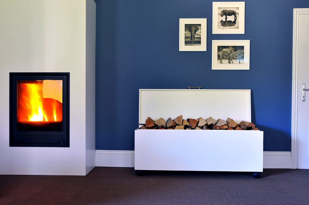 Idee per un soggiorno contemporaneo con pareti blu, cornice del camino in metallo, moquette, stufa a legna e pavimento marrone