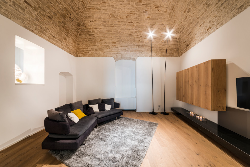 Esempio di un soggiorno mediterraneo con pareti bianche, pavimento in legno massello medio, pavimento marrone e TV a parete