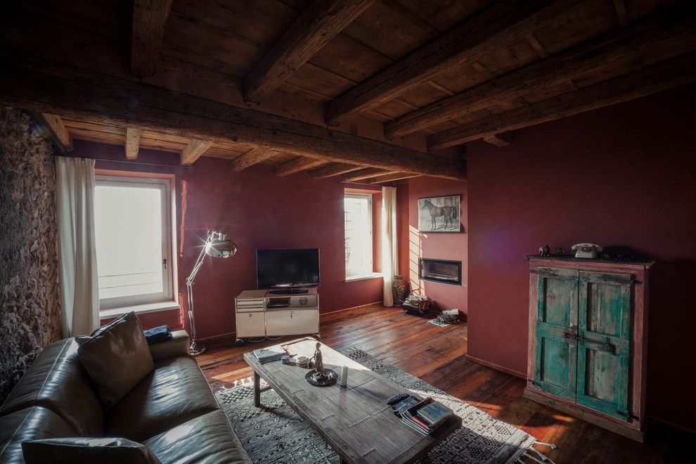 Mittelgroßes Landhaus Wohnzimmer im Loft-Stil mit braunem Holzboden, braunem Boden, roter Wandfarbe, Gaskamin und verputzter Kaminumrandung in Sonstige