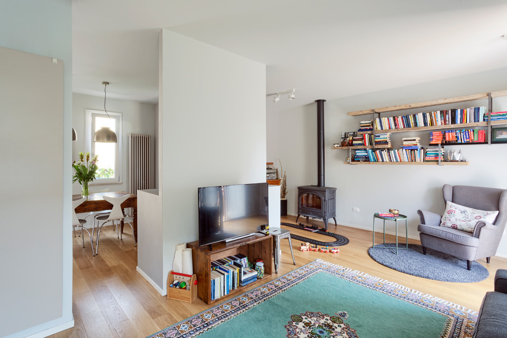 Stilmix Wohnzimmer mit grauer Wandfarbe, hellem Holzboden, Kaminofen, Kaminumrandung aus Metall, freistehendem TV und beigem Boden in Sonstige