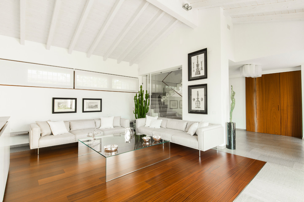 Inspiration pour un grand salon design ouvert avec un mur blanc et un sol en bois brun.