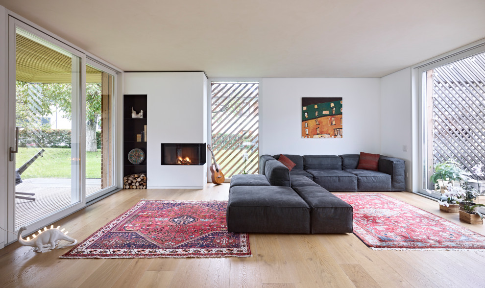 Offenes Modernes Wohnzimmer mit weißer Wandfarbe, braunem Holzboden, Eckkamin, verputzter Kaminumrandung, verstecktem TV und beigem Boden in Sonstige