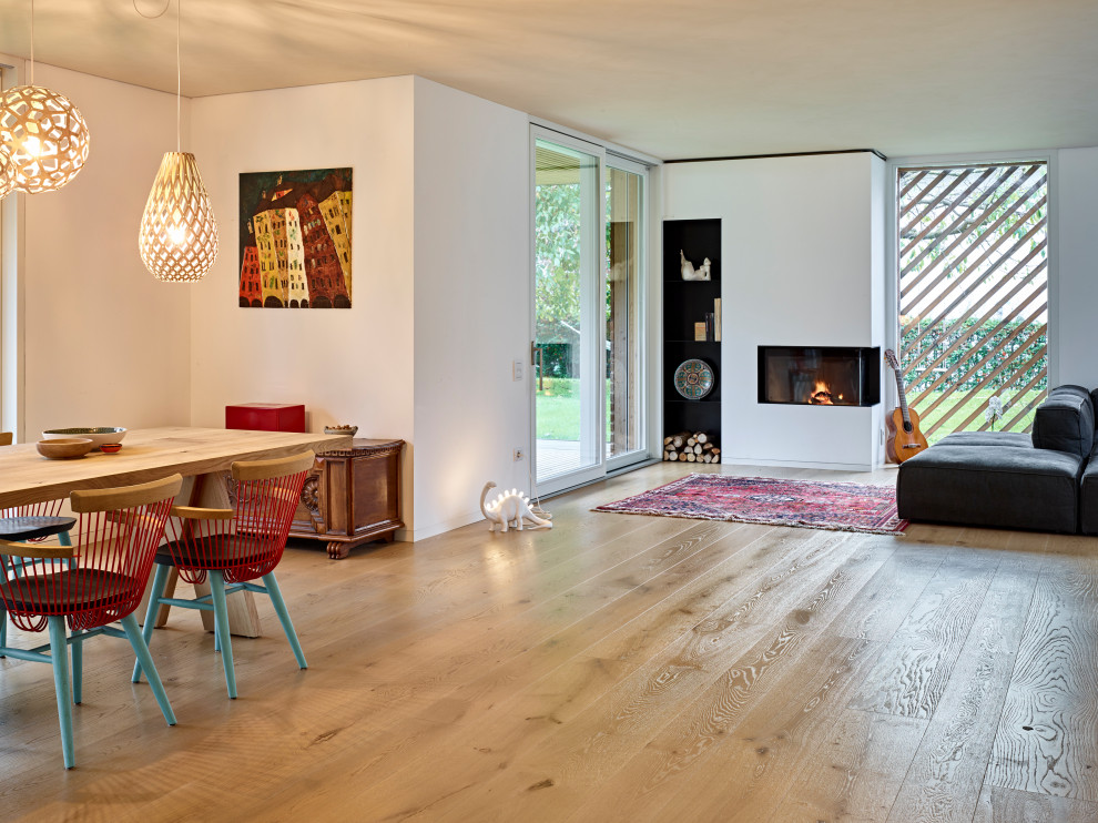 Offenes Skandinavisches Wohnzimmer mit weißer Wandfarbe, braunem Holzboden, Eckkamin, verputzter Kaminumrandung, verstecktem TV und beigem Boden in Sonstige